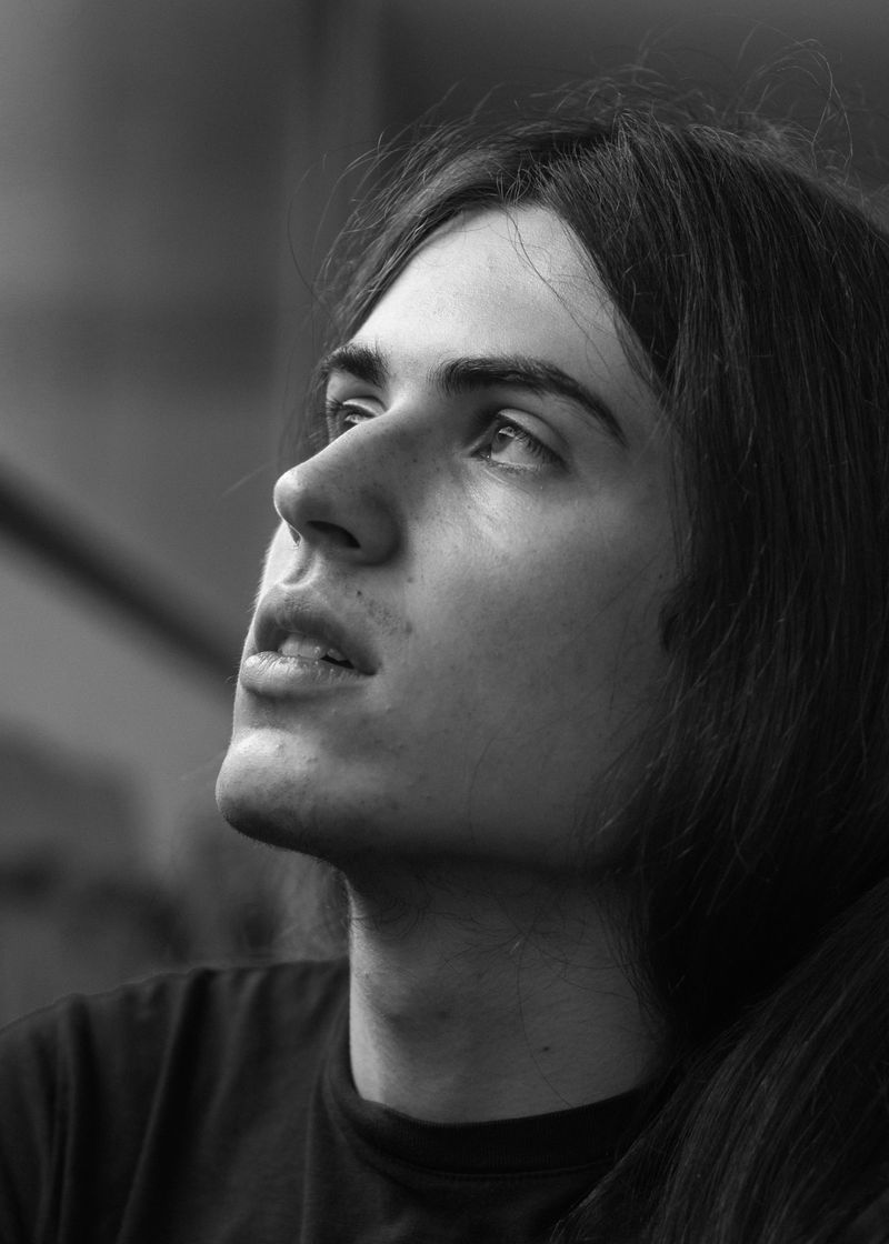 Black and white: a person with long hair, chin raised, looking up and away from the camera, blurred stair railings behind.