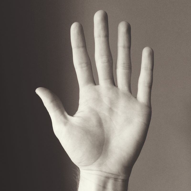Sepia-toned: an open palm and outstretched fingers held up against a plain wall, lit from one side.