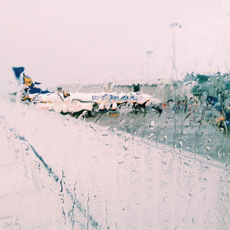 Airliners at their gates seen through an airplane window streaked with heavy rain.