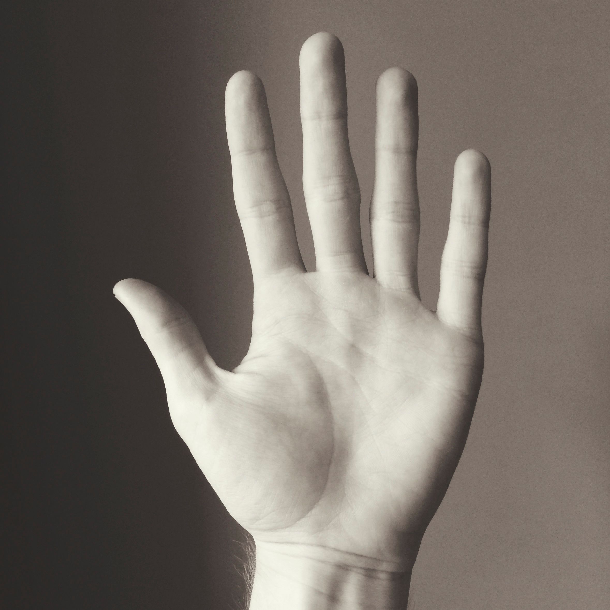 Black and white: an open palm held up to the camera against a plain grey wall, fingers spread.