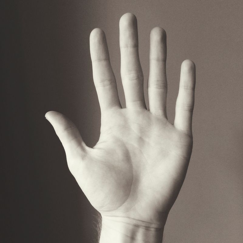 Black and white: an open palm held up to the camera against a plain grey wall, fingers spread.